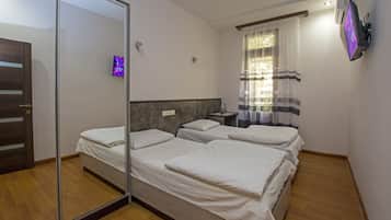 A hotel room with three beds, a large mirror, a TV, and a window with curtains.