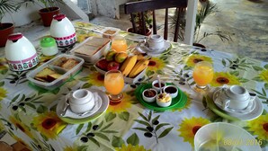 A table set with breakfast items including bread, fruits, and beverages, with a floral tablecloth. - Casa Nostra Hospedagem Residencial (Cabo Frio)