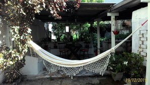A hammock under a wooden pergola with a stone patio, surrounded by potted plants and a table with chairs. - Casa Nostra Hospedagem Residencial (Cabo Frio)