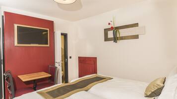 A hotel room with a bed, a small table, a chair, a mirror, and a red wall.