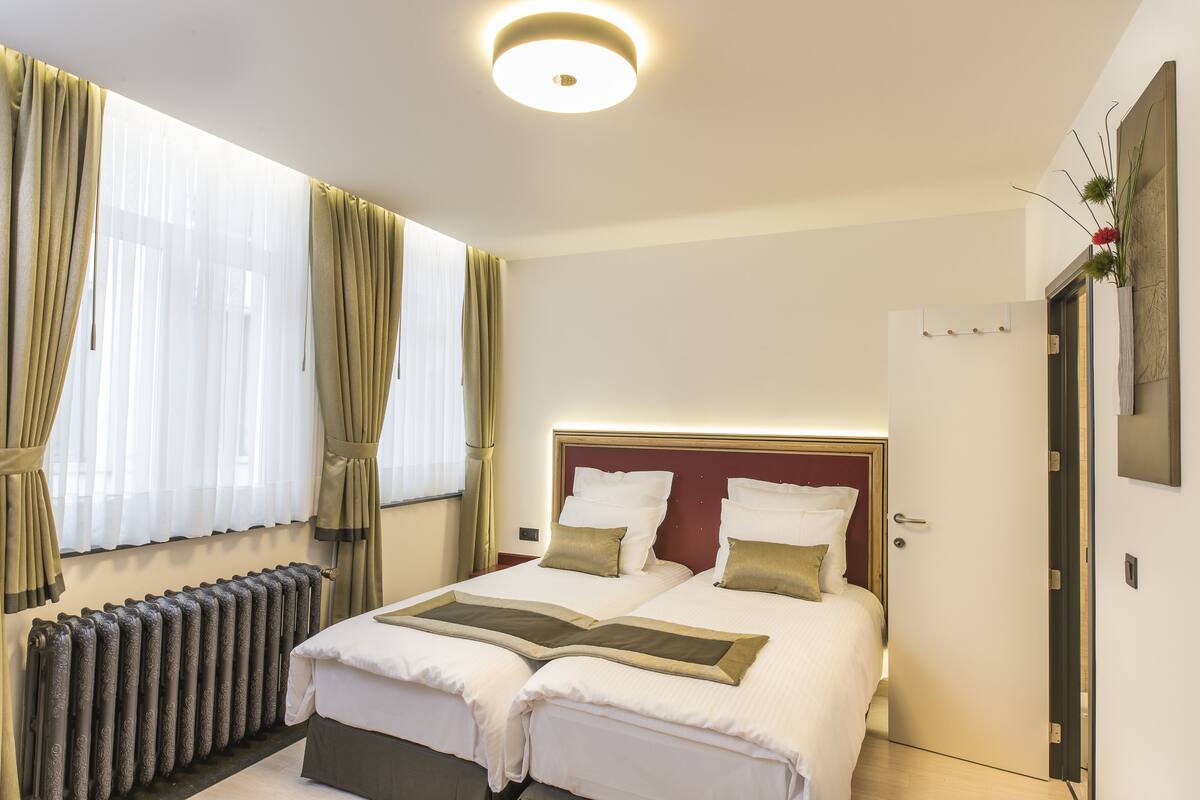 Habitación de hotel con una cama grande, un radiador, cortinas y una puerta.