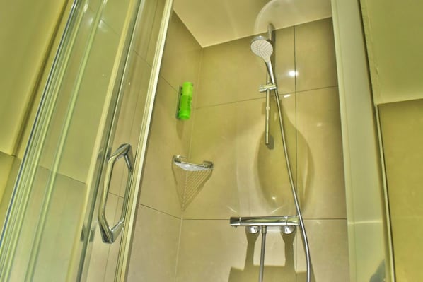 Ein modernes Badezimmer mit Duschkabine aus Glas, einer Handbrause und einer grünen Flasche an der Wand.