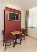 A small room with a red accent wall, a wooden table, two red chairs, and a black-framed mirror.