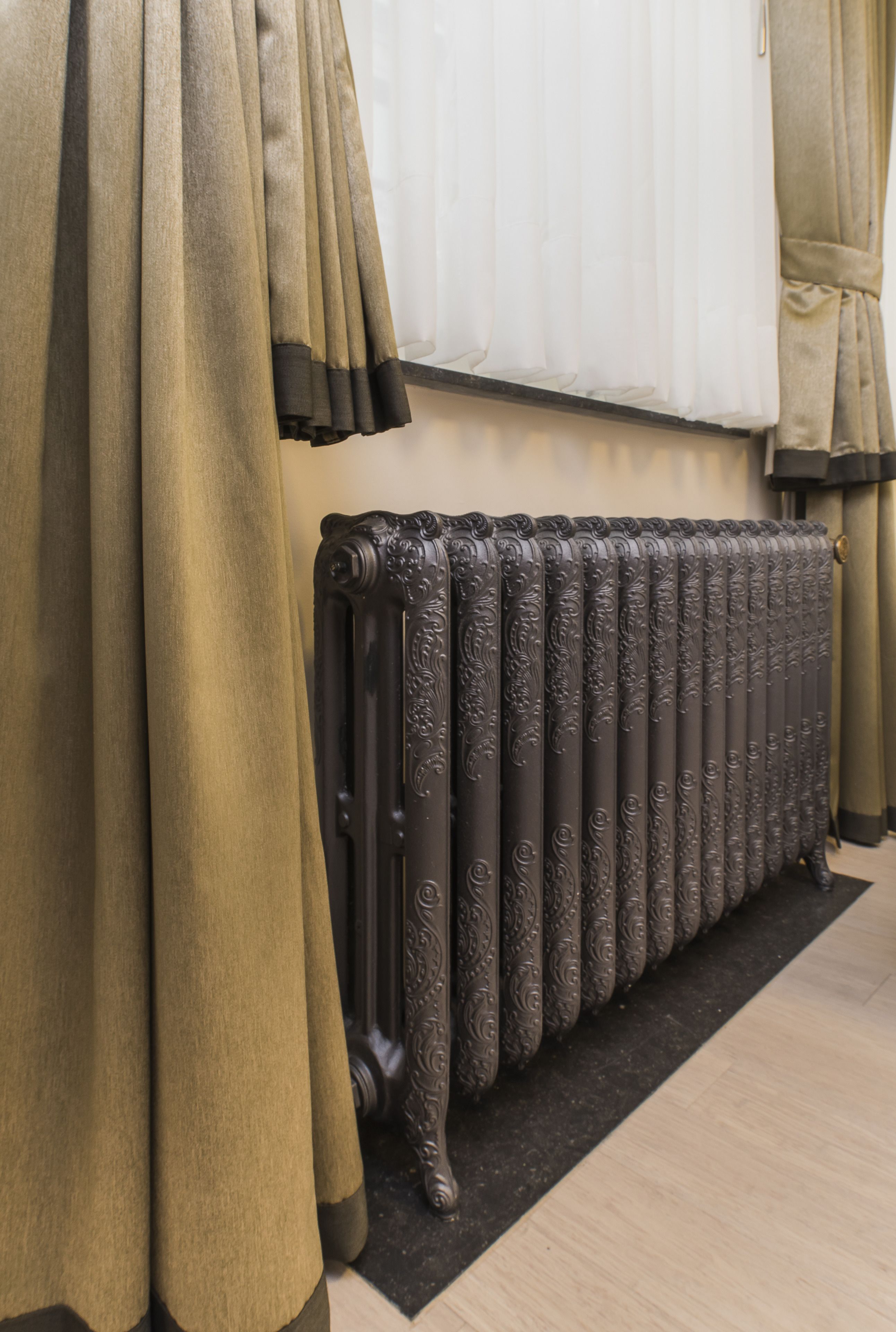 Een radiator met gedetailleerde versieringen, gordijnen en een vloerbedekking.