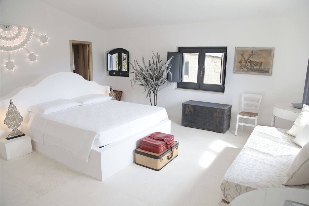 A bedroom with a large bed, bedside tables, a desk, a chair, and a window.