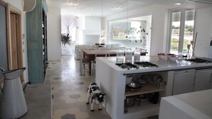 A modern kitchen with a central island, a dining area with a wooden table, and a view of the outdoors.