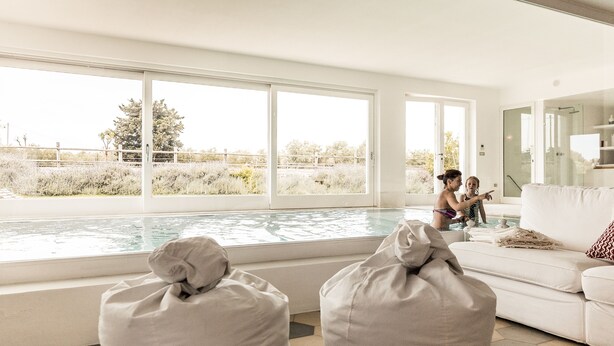 A modern living room with a large window overlooking a swimming pool, a white couch, and two bean bags.