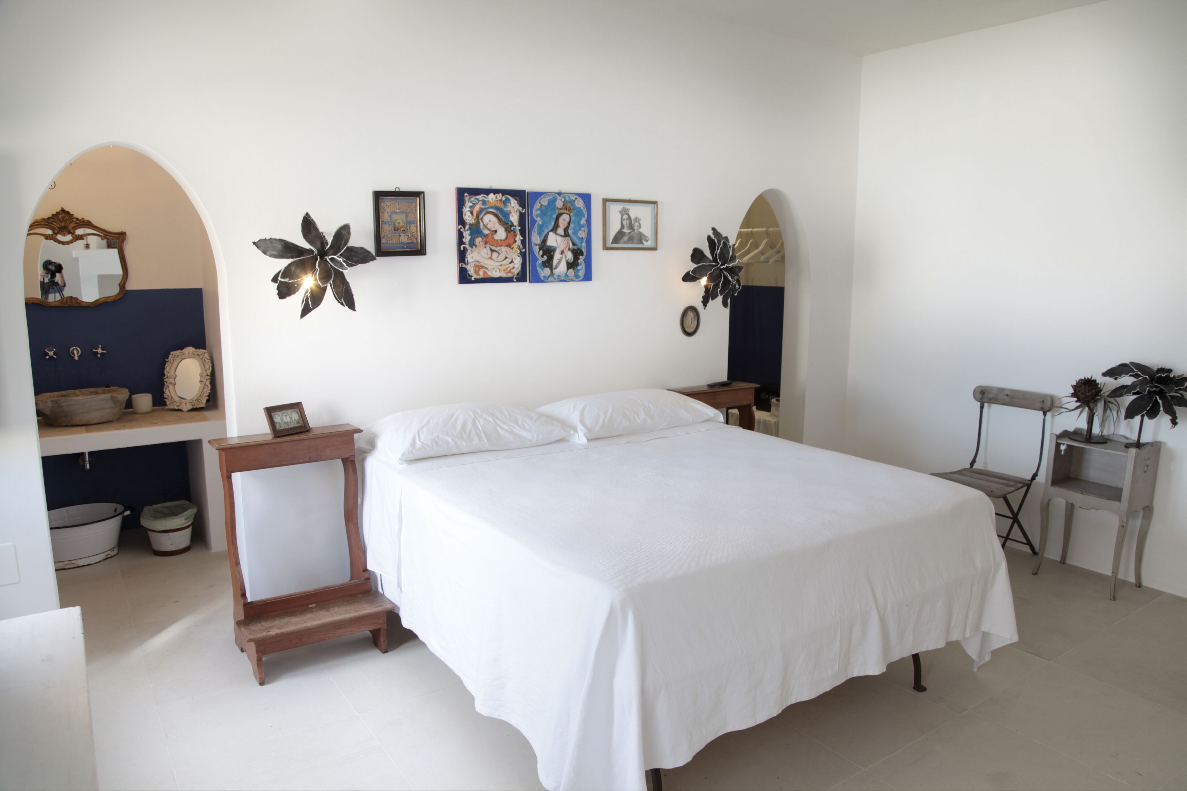 Une chambre à coucher avec un grand lit, une petite table, une chaise et une étagère ornée d’objets décoratifs.