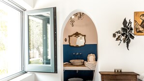 A bathroom with a window, a mirror, a sink, and a small table.