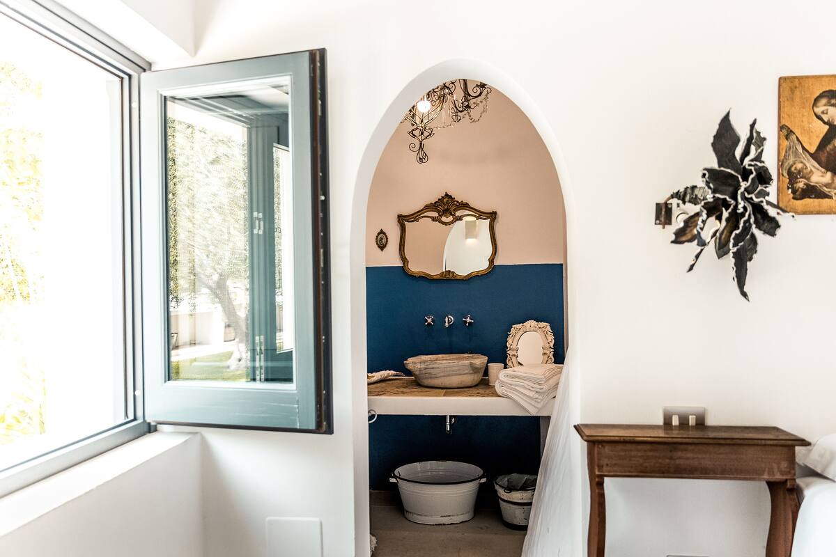 A bathroom with a window, a mirror, a sink, and a small table.