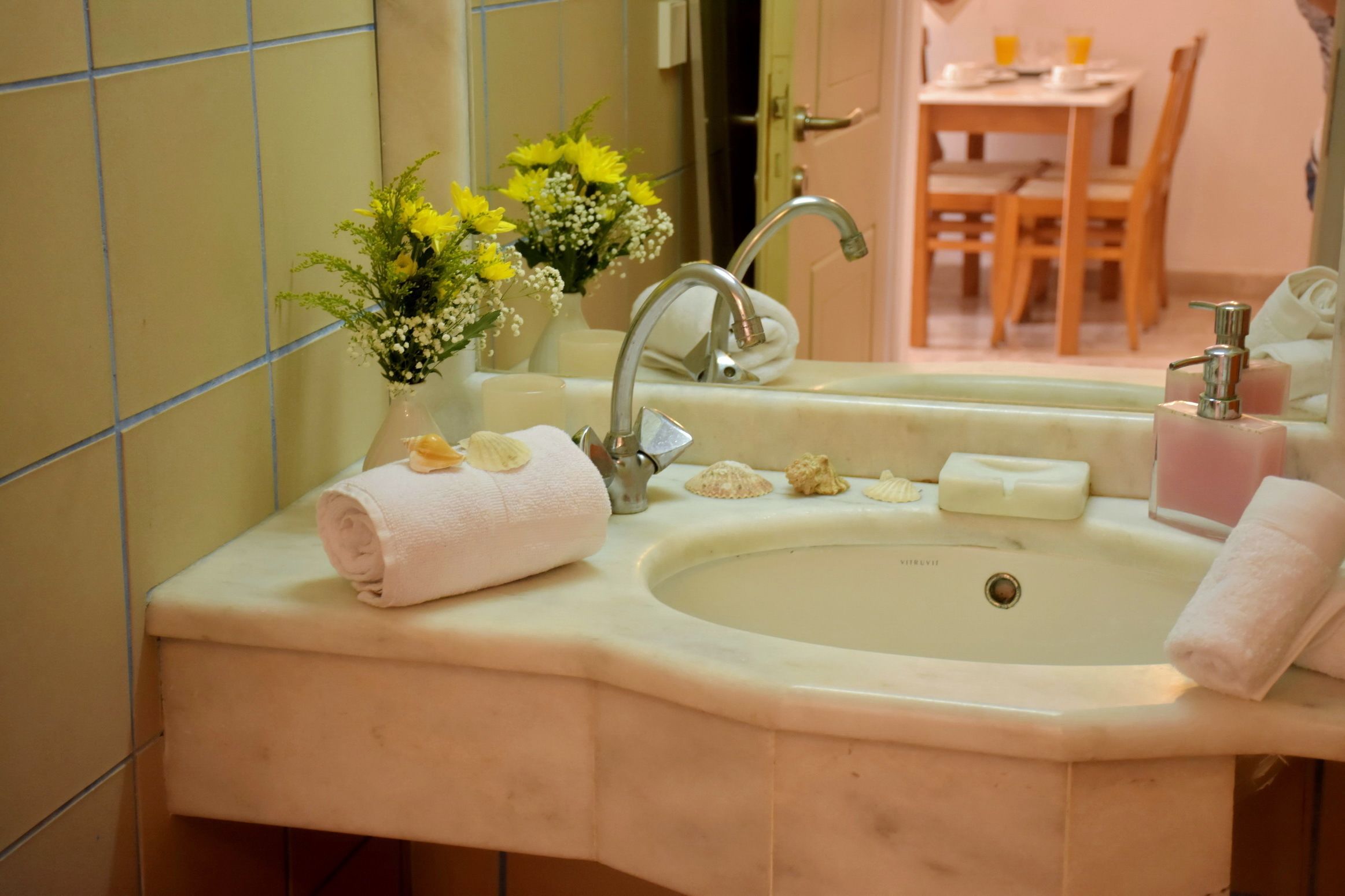 A bathroom with a sink, mirror, and a vase with yellow flowers.