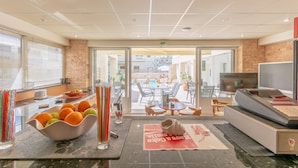A hotel lobby with a reception desk, a dining area with tables and chairs, and a pool area visible through the glass doors. - Irini Apartments (Hersonissos)