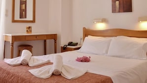 A hotel room with a bed, a desk, a chair, a mirror, and a painting on the wall. - Irini Apartments (Hersonissos)