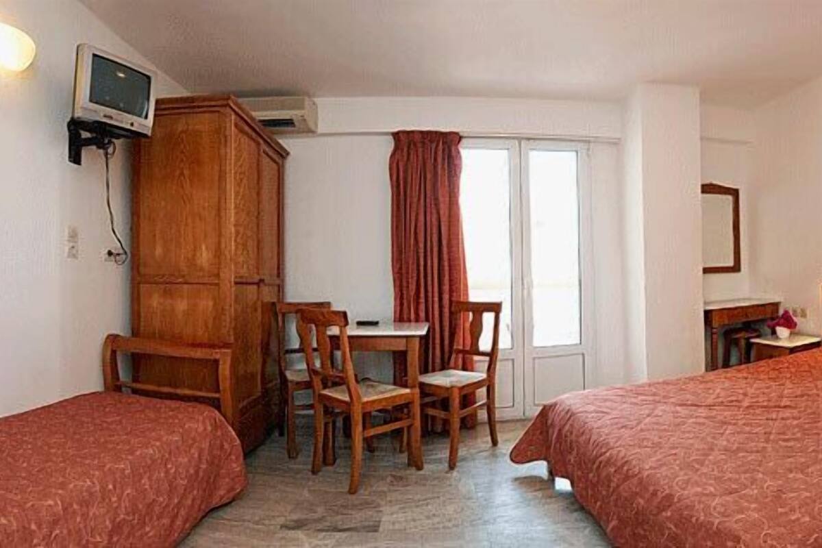 A hotel room with two beds, a desk with chairs, a television, and a window with curtains.