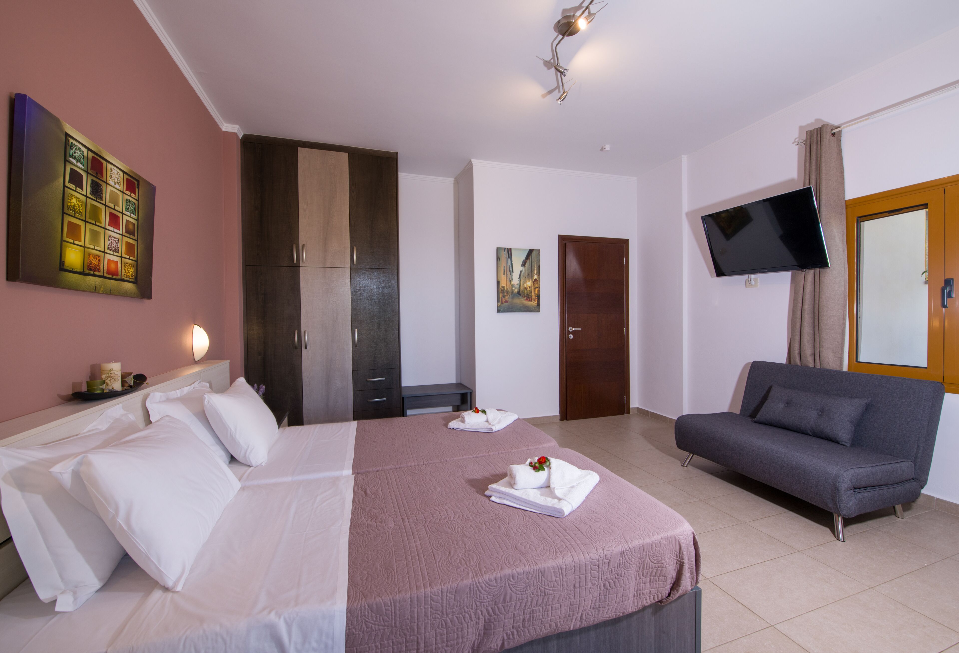 A hotel room with a large bed, a sofa, a TV mounted on the wall, and a wardrobe.