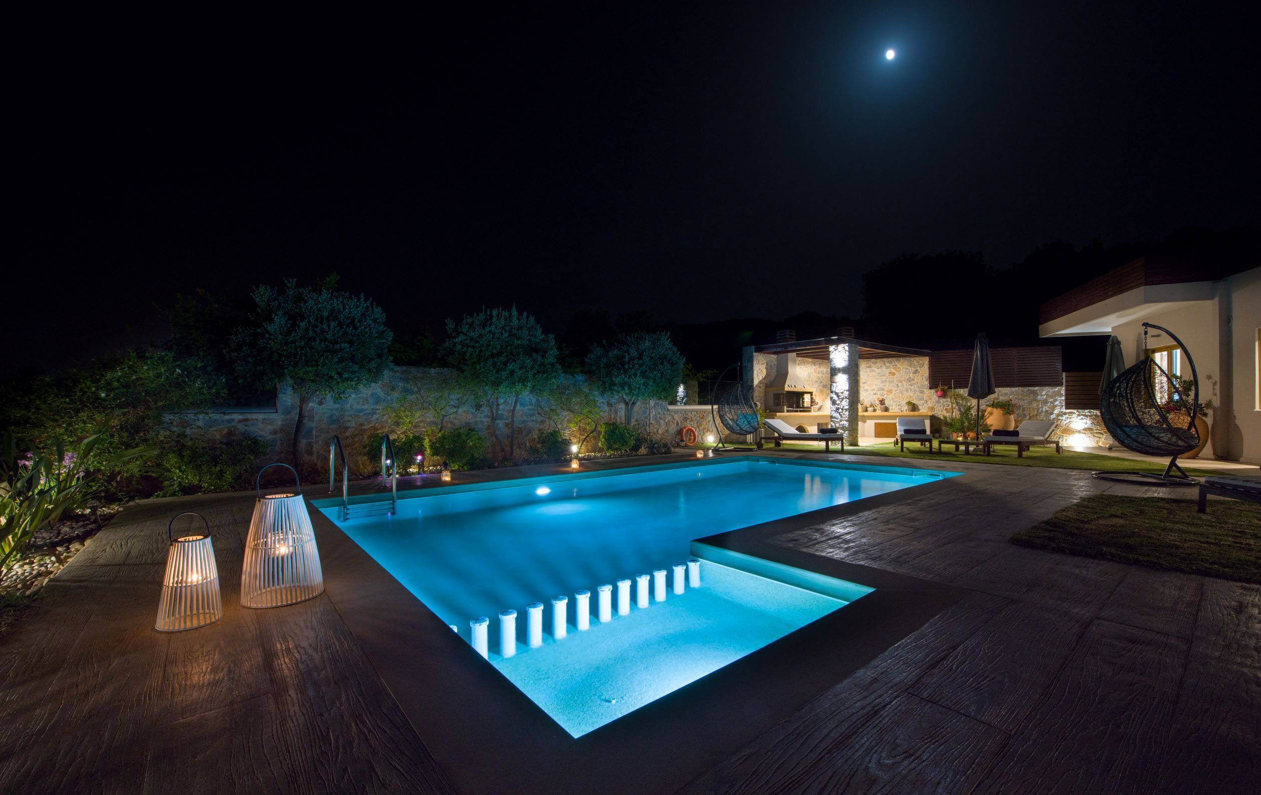 Una piscina con una pared de piedra y una hamaca colgante, rodeada de árboles y un edificio de piedra.