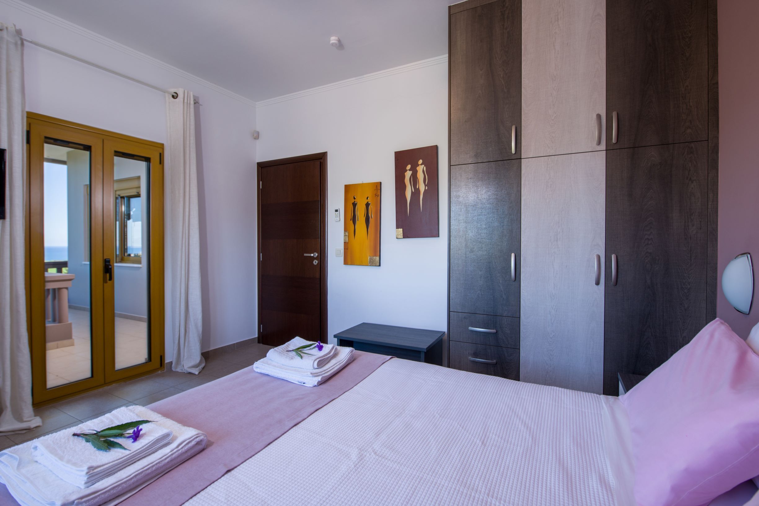 A bedroom with a bed, a wardrobe, a desk, and a door leading to a balcony.