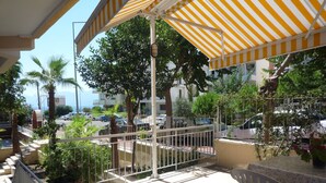 A balcony with a striped awning, potted plants, and a view of parked cars and buildings. - Pinus Otel (Antalya)