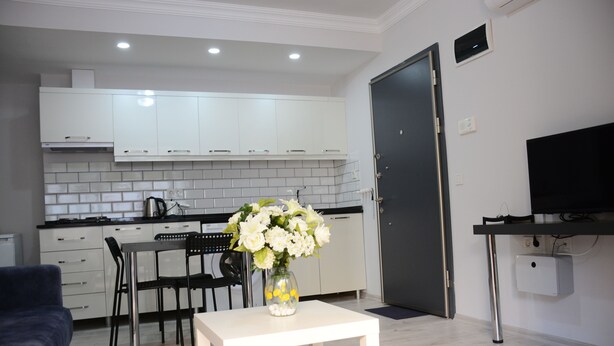 A modern kitchen with white cabinets, a dining area with a white table and chairs, and a TV on a stand. - Pinus Otel (Antalya)