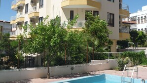 A multi-story building with balconies, a swimming pool, and surrounding greenery. - Pinus Otel (Antalya)
