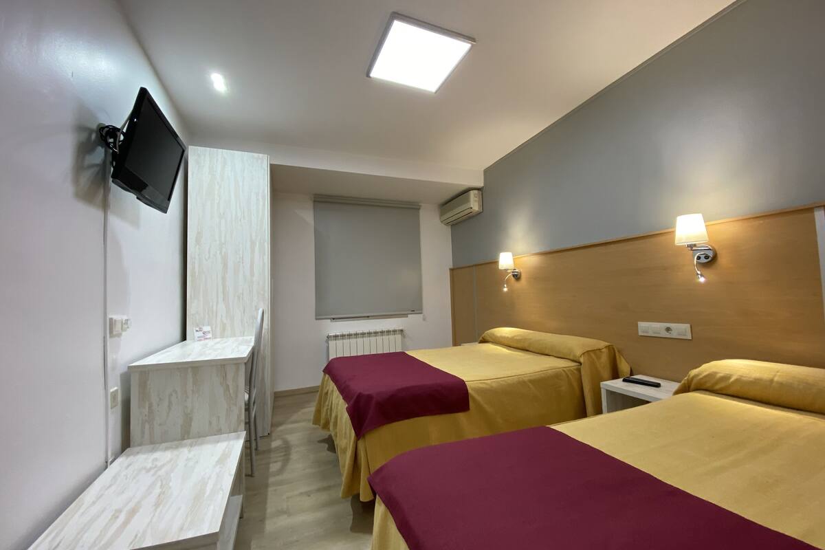 Een hotelkamer met twee bedden, een aan de muur bevestigde televisie en een klein bureau.