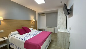 Habitación de hotel con cama, mesitas de noche, televisor montado en la pared y una ventana con persianas.