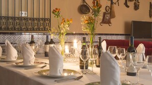Mesa de comedor preparada con servilletas blancas, platos y cubiertos, además de botellas de vino y un jarrón con flores.