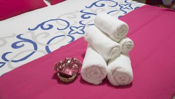 Un lit bien fait, avec une literie rose et blanche, un panier rempli de produits de toilette et des serviettes enroulées.