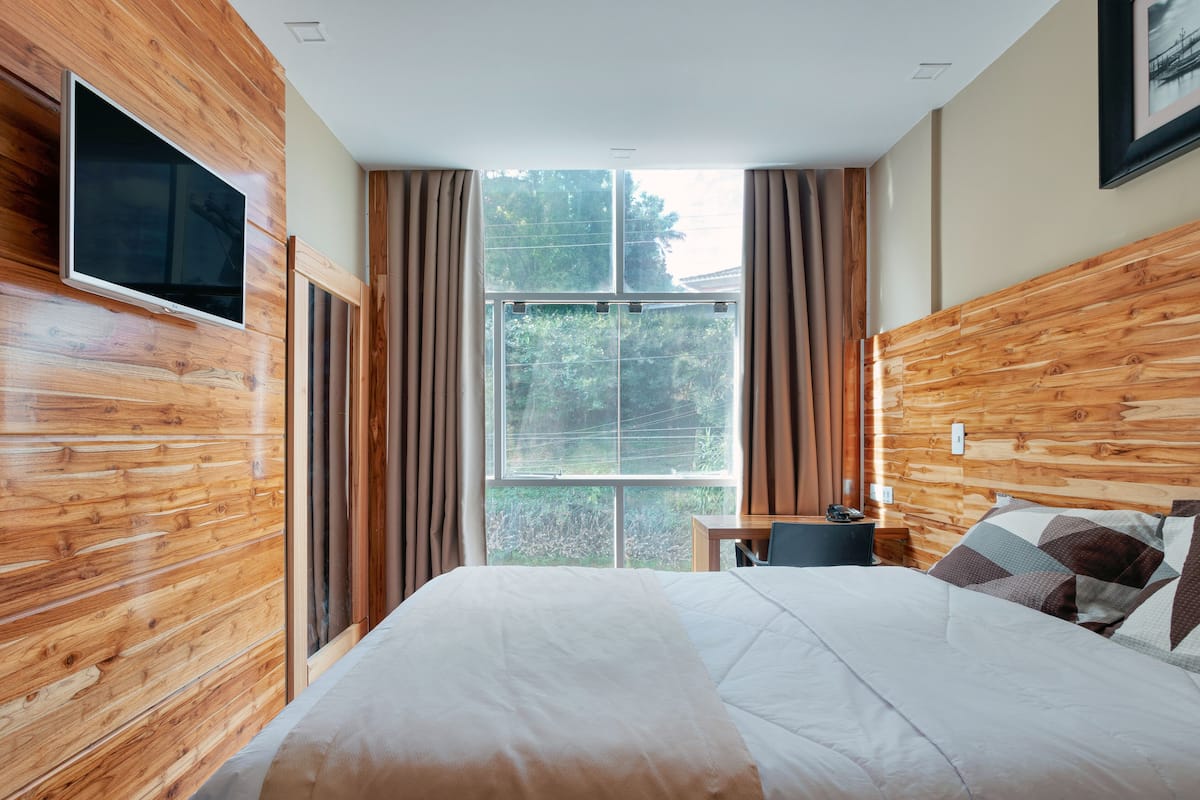 Un dormitorio con una cama grande, paredes de madera, una ventana con cortinas y un televisor de pantalla plana montado en la pared.