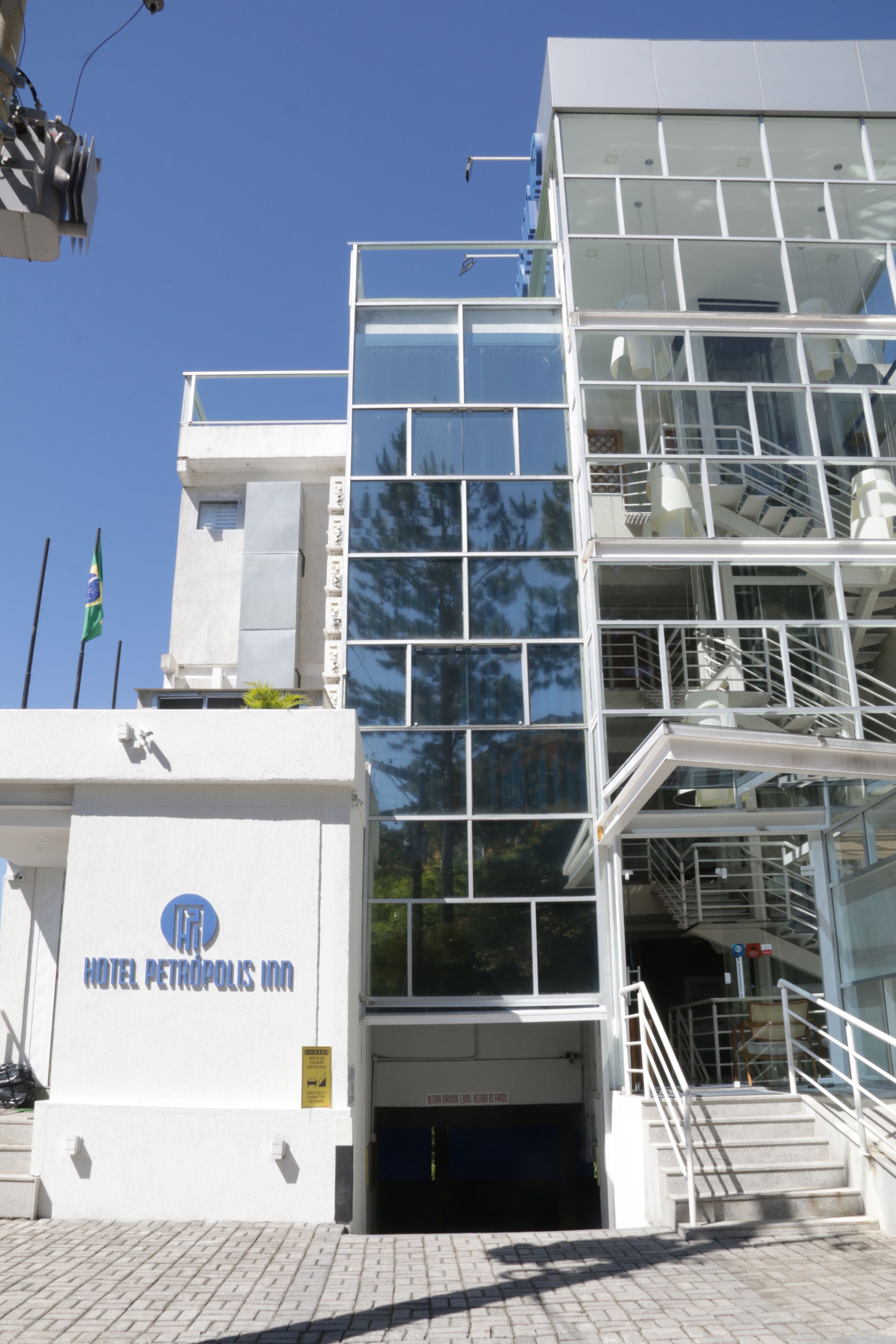 A modern hotel with a glass facade, a visible staircase, and a sign reading "HOTEL PETROPOLIS INN".