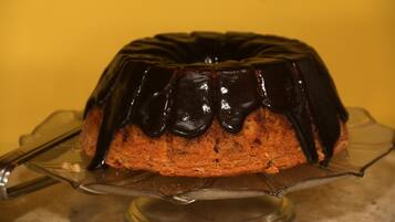 A bundt cake with chocolate glaze on a clear glass cake stand.