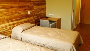 Habitación de hotel con dos camas, un cabecero de madera, un escritorio pequeño con una silla y una puerta que da a otra habitación.