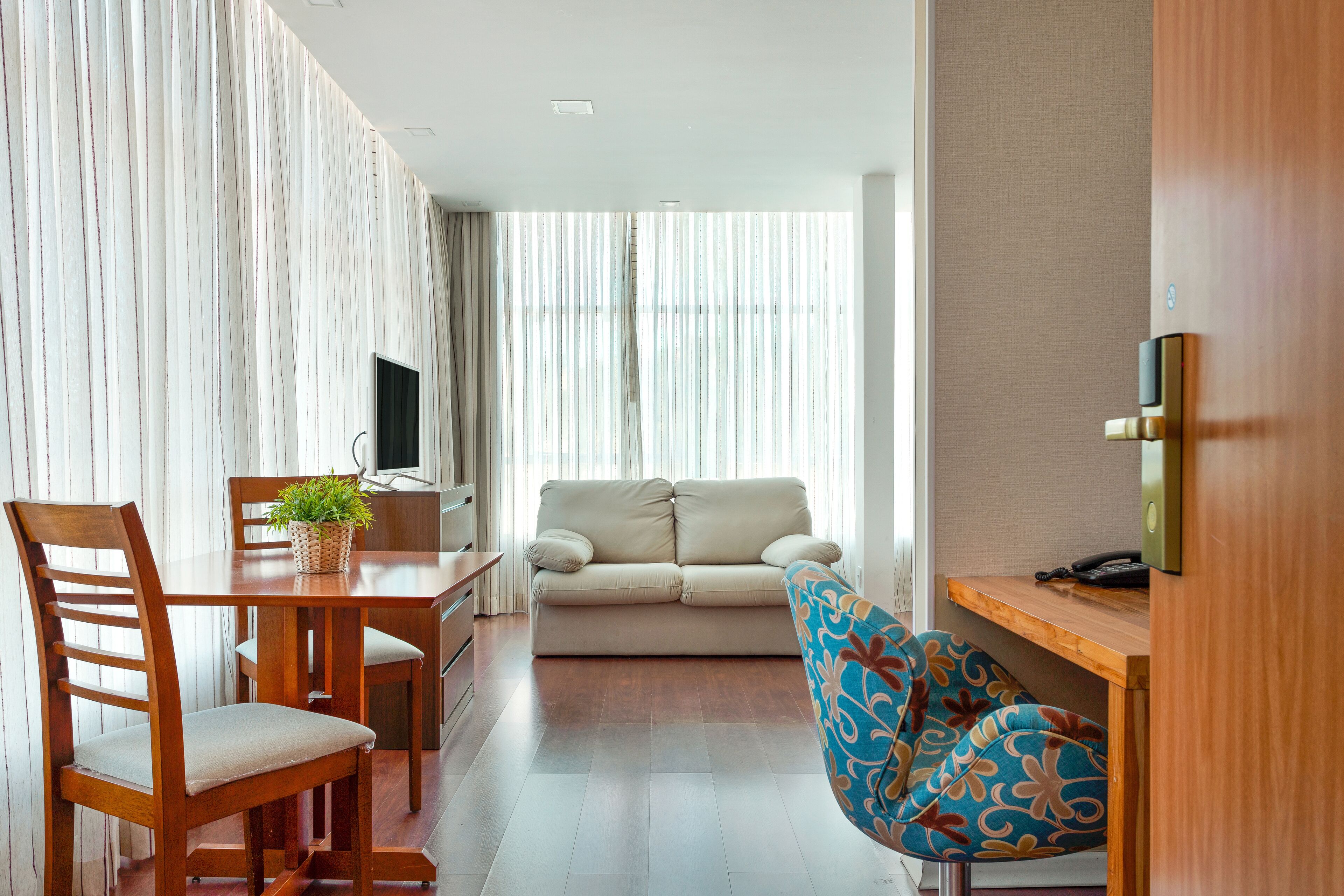 A modern living room with a wooden dining table, a beige sofa, and a patterned armchair.