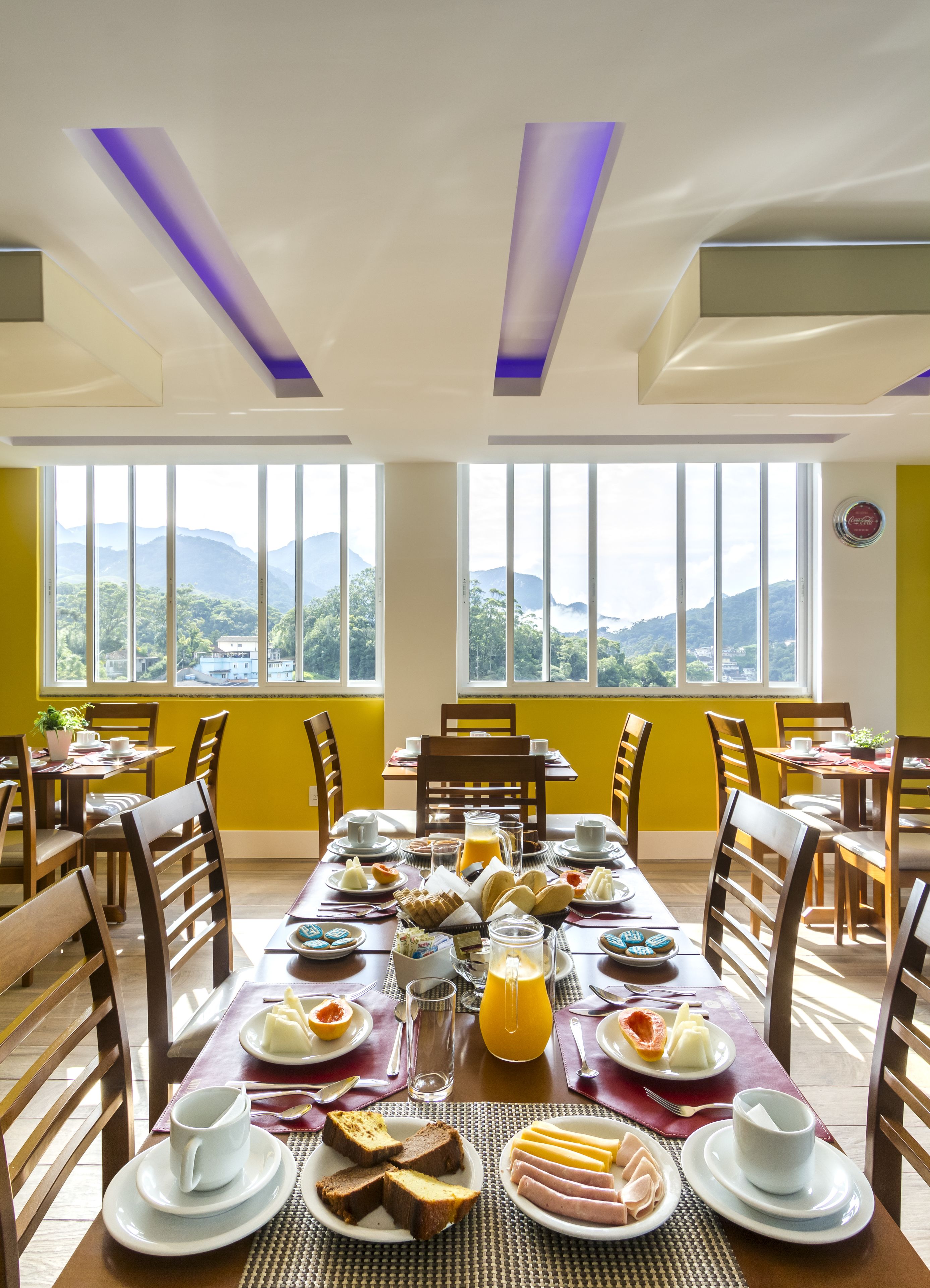 Un comedor con una mesa dispuesta para el desayuno, mostrando platos de comida, tazas y un vaso de jugo de naranja.