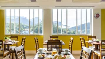 Un comedor con una mesa dispuesta para el desayuno, mostrando platos de comida, tazas y un vaso de jugo de naranja.
