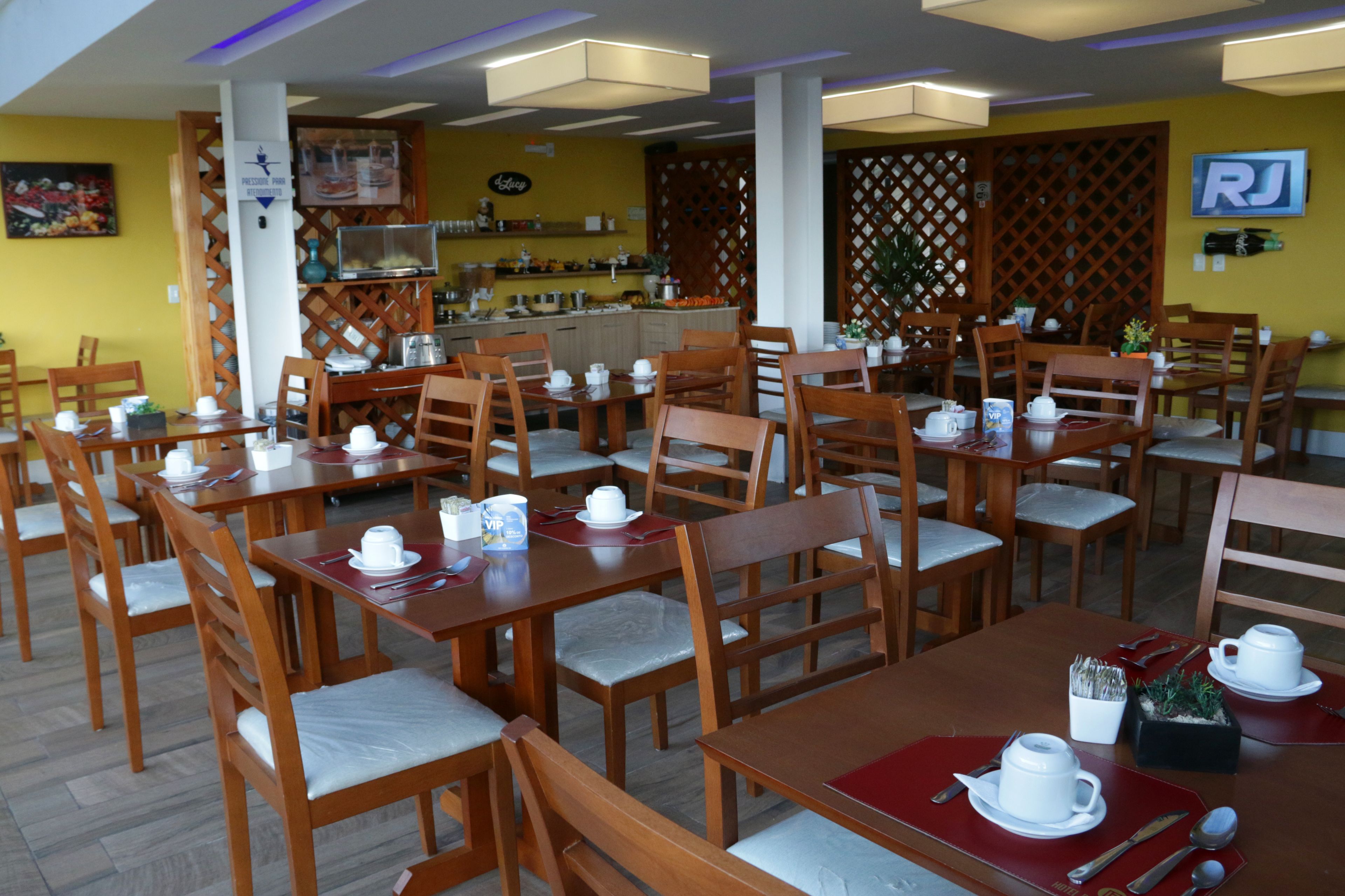 A restaurant with wooden tables and chairs, a bar area, and a yellow wall with a sign.
