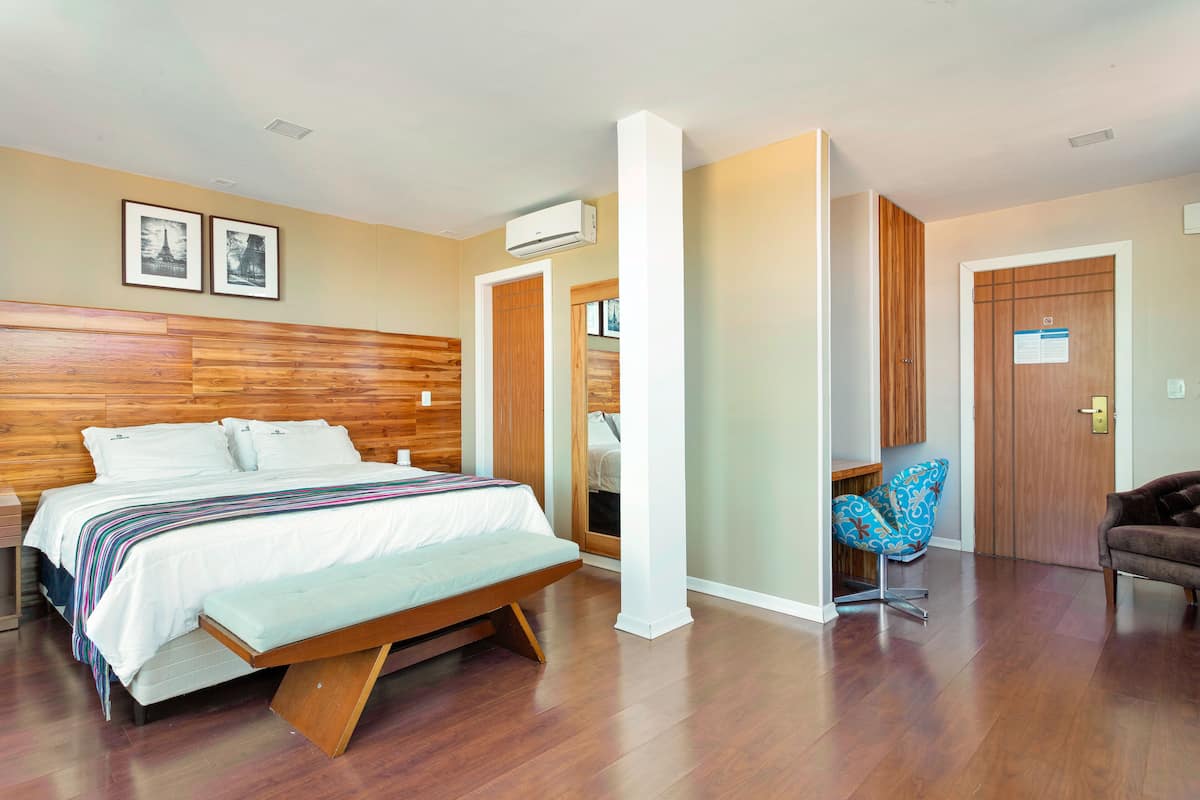 Un dormitorio moderno con cabecera de madera, una cama con manta a rayas, un banco, una silla azul y una puerta de madera.