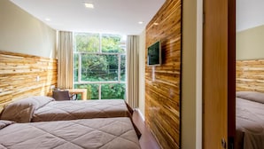 Habitación de hotel con dos camas, un televisor montado en la pared y ventana con vistas a zonas verdes.