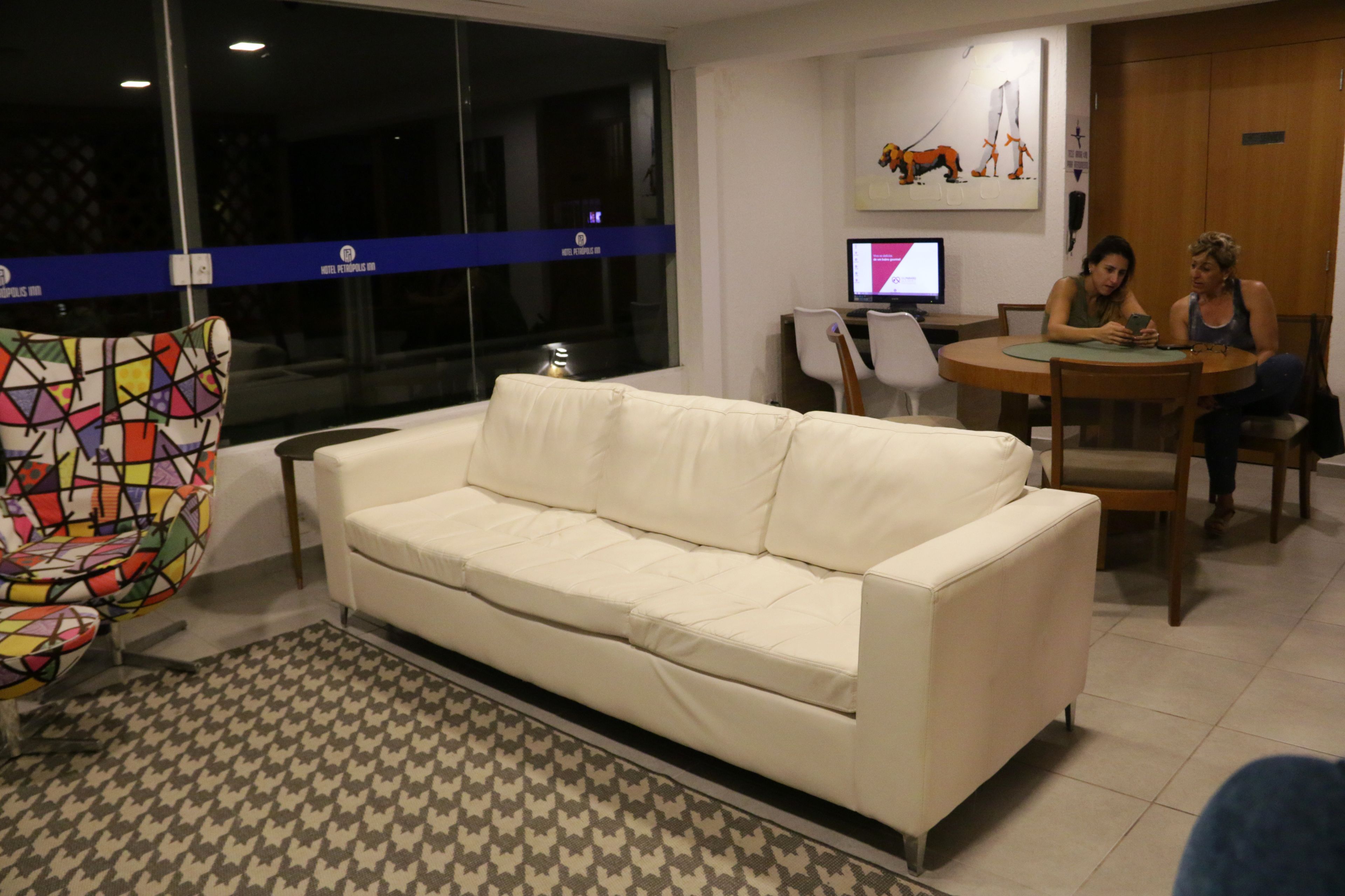 A living room with a white sofa, a colorful chair, a patterned rug, and a dining area with a table and chairs.