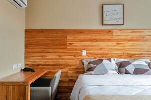 A bedroom with a wooden headboard, a bed with patterned pillows, a bedside table with a phone, and a motivational quote on the wall.