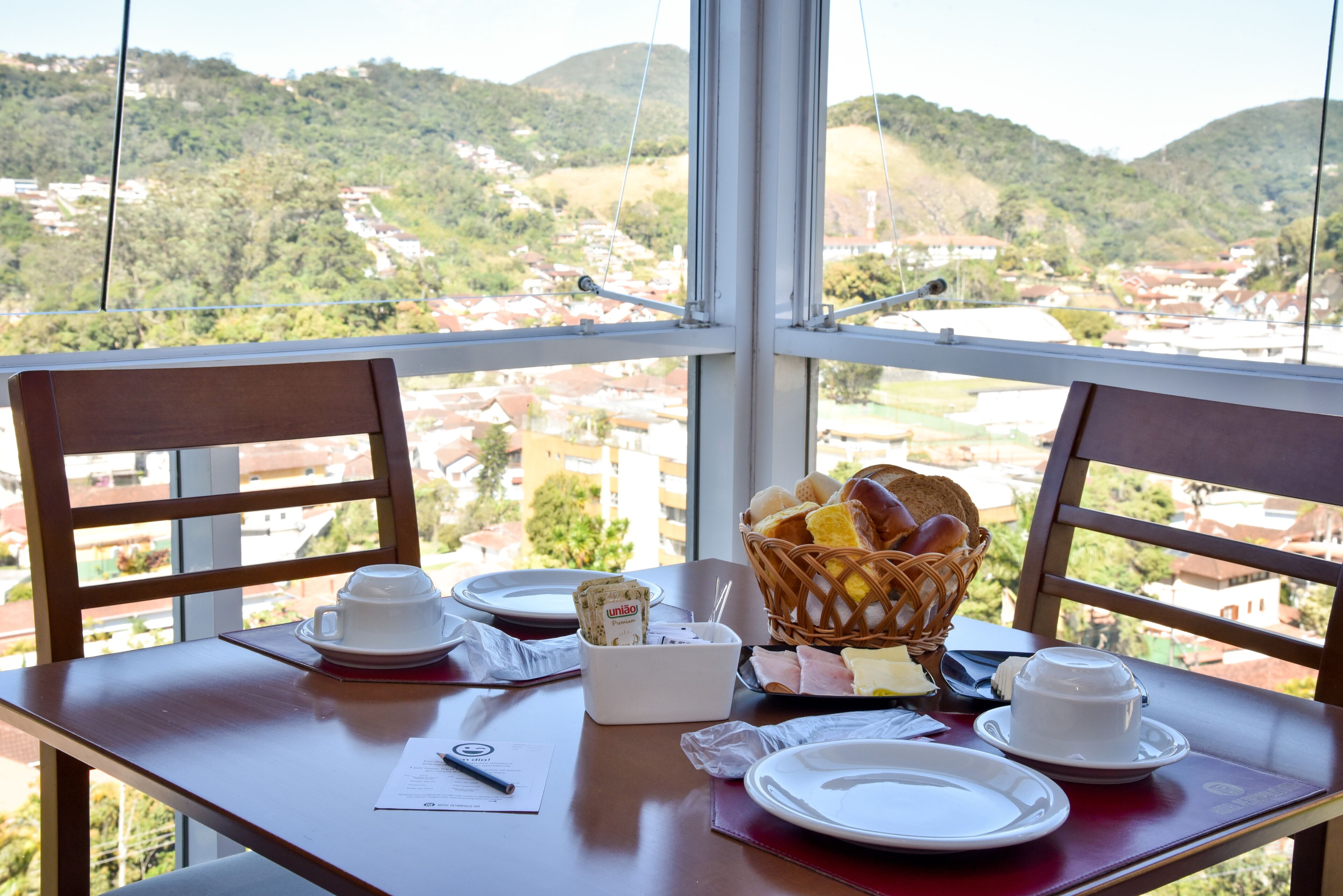 Una mesa de comedor con vistas a un paisaje montañoso, una cesta de pan y una taza de café.