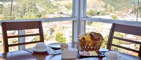 Una mesa de comedor con vistas a un paisaje montañoso, una cesta de pan y una taza de café.
