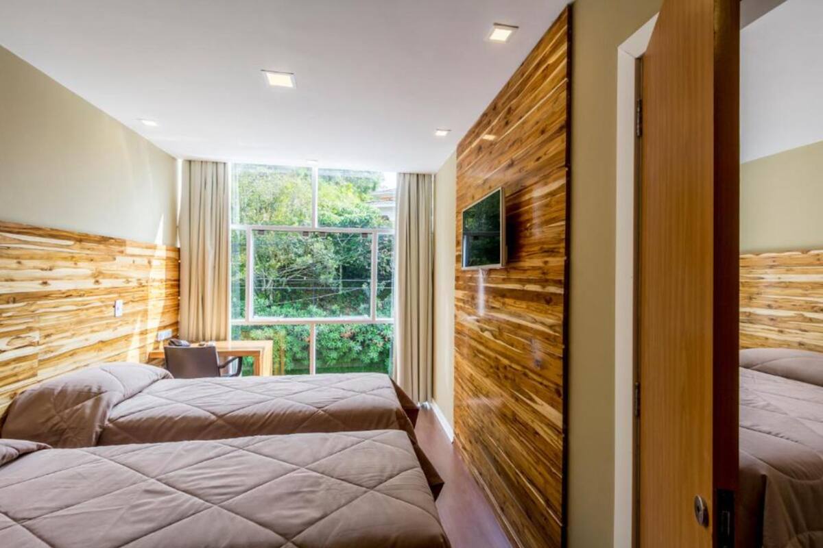 Habitación de hotel con dos camas, un televisor montado en la pared y una ventana con vistas a zonas verdes.