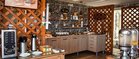 Una estación de café con varias cafeteras, un dispensador de café y una variedad de tazas y pasteles.