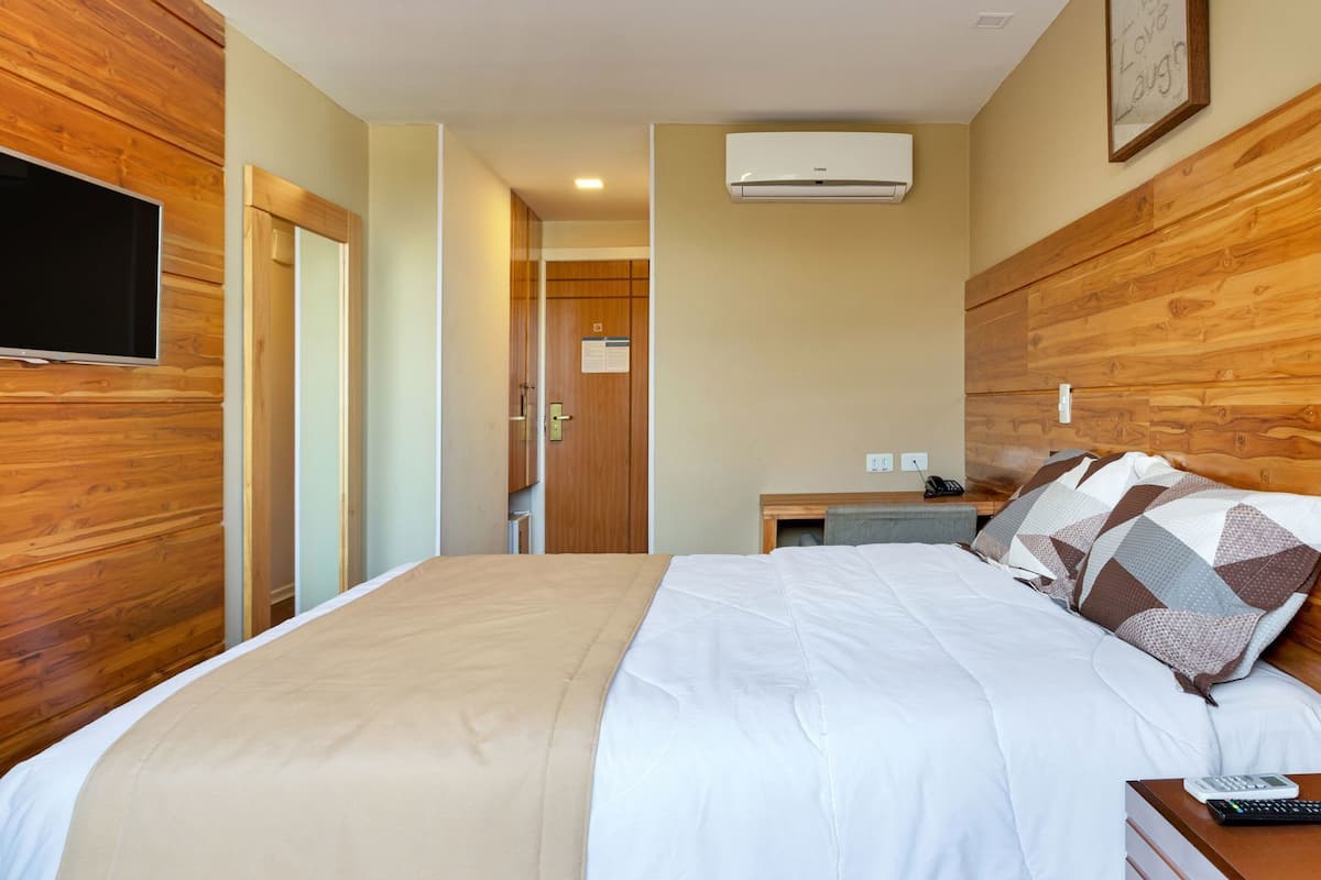 Una habitación de hotel con cama, mesita de noche y televisión montada en la pared.