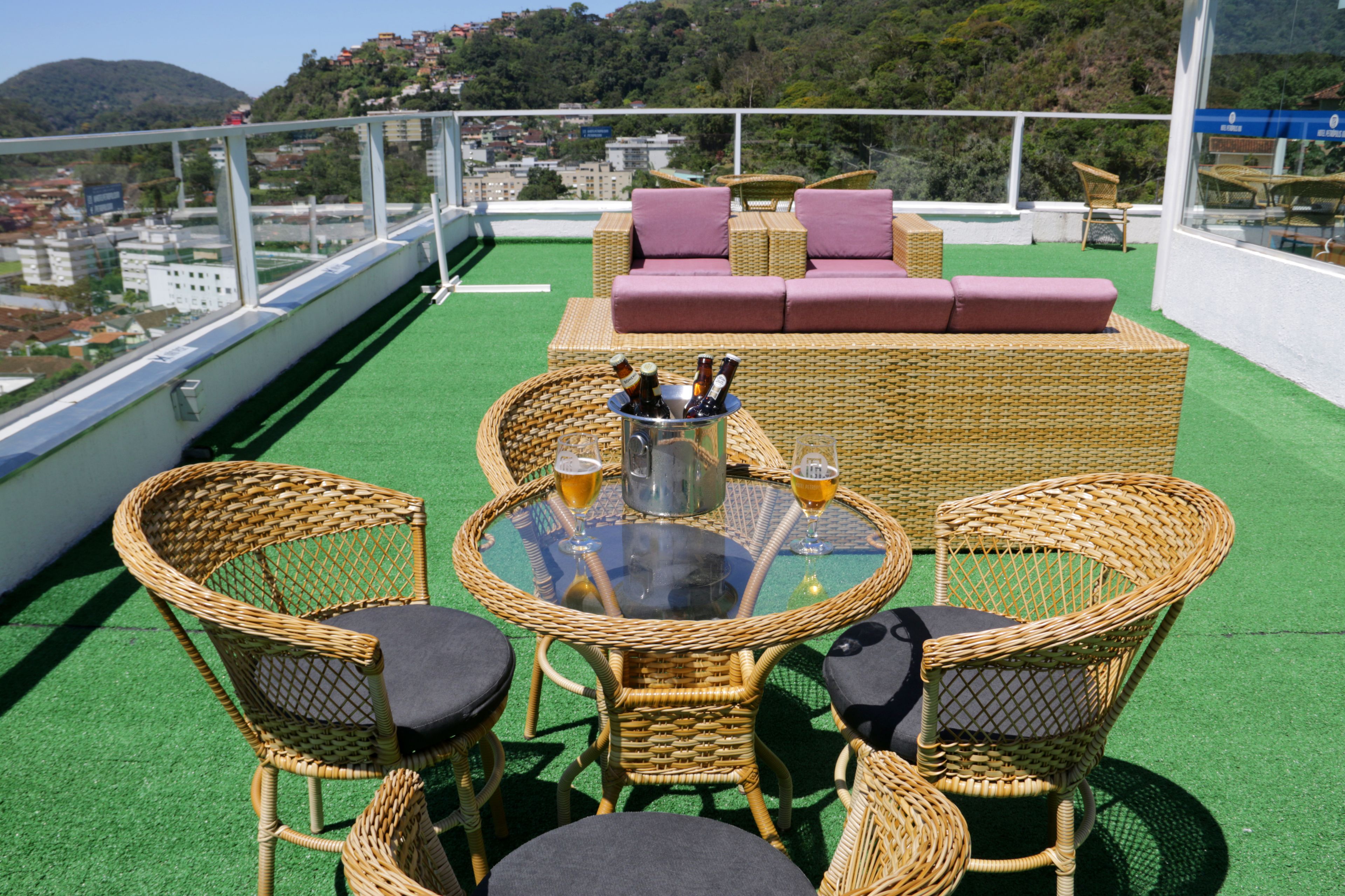 A rooftop terrace with wicker furniture, a glass table, and a bottle of beer.