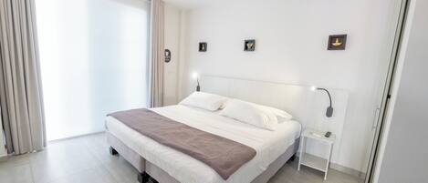 A modern bedroom with a large bed, a bedside table, a ceiling fan, and a sliding door.