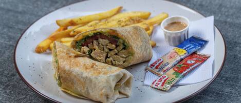 Un plato con un wrap, papas fritas y salsas.