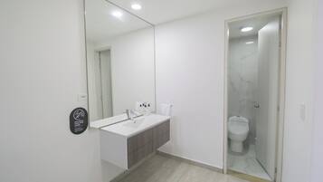 Un baño moderno con lavamanos, espejo y retrete blancos.
