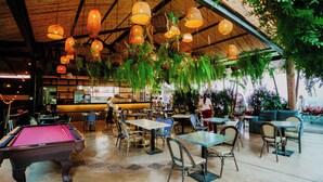 An indoor dining area with tables and chairs, a pool table, hanging lights, and greenery. - Viajero Cali Hostel & Salsa School (Cali)